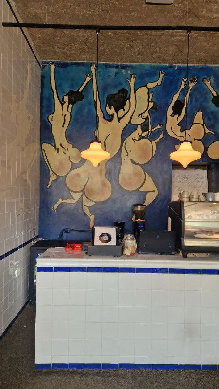 Барная стойка на тёмной стороне заведения на фоне большого настенного панно с актами в динамике, висящее теплое освещение создает уют.