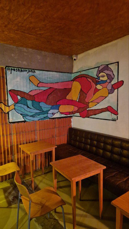 Уютный уголок с кожаным диваном и настенным графическим полотном с яркими цветами, деревянные столы и мягкие лампы создают камерную атмосферу.