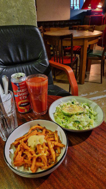 Тарелки со стритфуд‑вариациями: салат, сладкий картофель фри и напитки на столе бара, видно сочетание простого меню и атмосферной подачи.