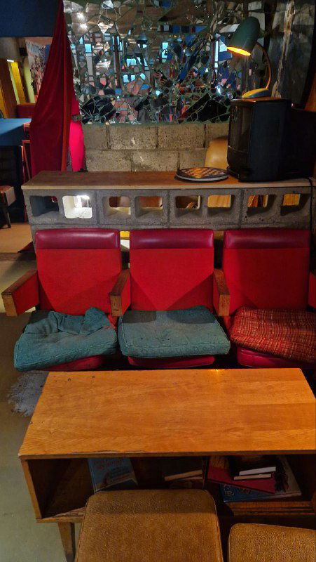 Низкие красные сиденья и зеркальная декоративная панель за столом, мягкие подушки и предметы винтажной мебели создают эклектичный интерьер.