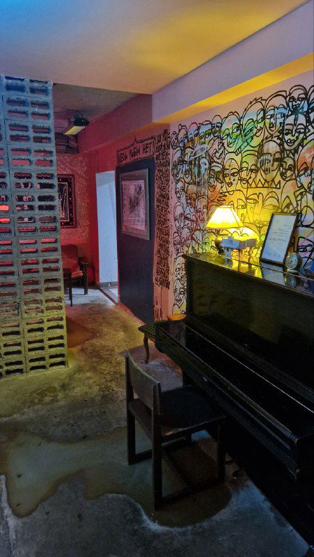 Проход с граффити на стенах, старое пианино и мягкое желтое освещение — часть неформальной эстетики бара, где выставляют современное искусство.