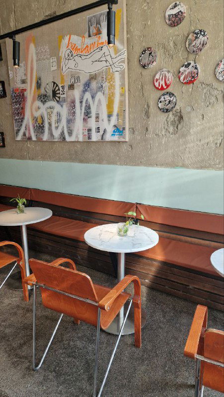 Уголок с длинной лавкой, столиками и современными настенными работами на текстурной стене — ещё одна сцена для сменных экспозиций в баре.