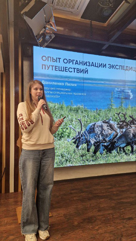 Докладчица на фоне слайда «Опыт организации экспедиционных путешествий», доклад о логистике и программе экспедиций Водохода.