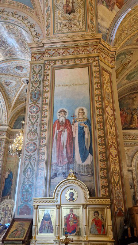 Фрагмент росписи и колонны внутри храма: яркие фрески, орнаментальные узоры и нижняя часть иконостаса с иконами и золочёными деталями.