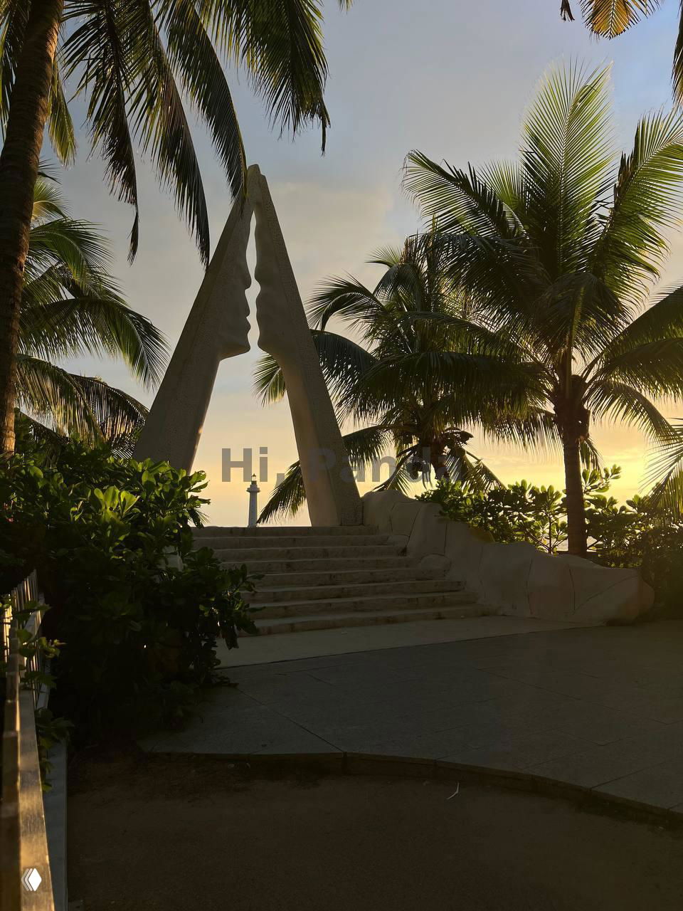 Силуэт декоративной арки и пальмы на фоне заката в Санья, тёплый свет солнца и тропическая растительность вокруг памятника у моря.