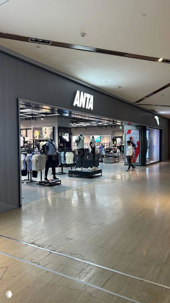 Магазин ANTA с открытым входом и выставленными товарами: интерьер спортивной торговой точки вдоль коридора торгового центра.