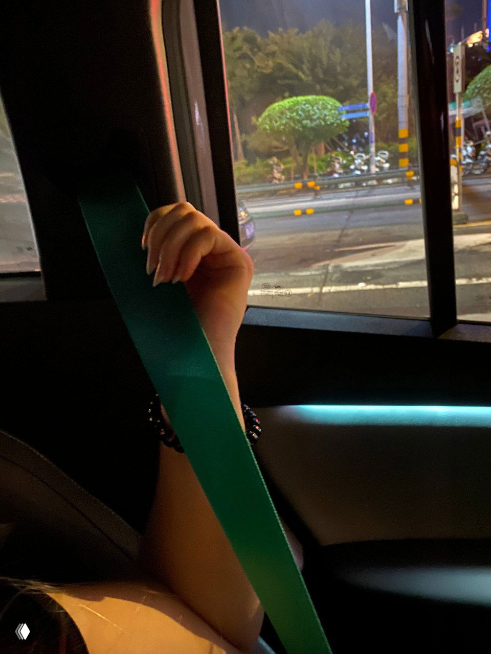 Крупный план на ремень безопасности зелёного цвета на фоне руки пассажира и бокового стекла — демонстрация элементов безопасности в салоне автономного такси.