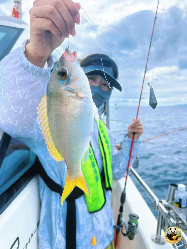 Человек в жилете и маске показывает пойманную рыбу на фоне палубы и моря; видны леска и лодочное оборудование, атмосфера морского рейса.