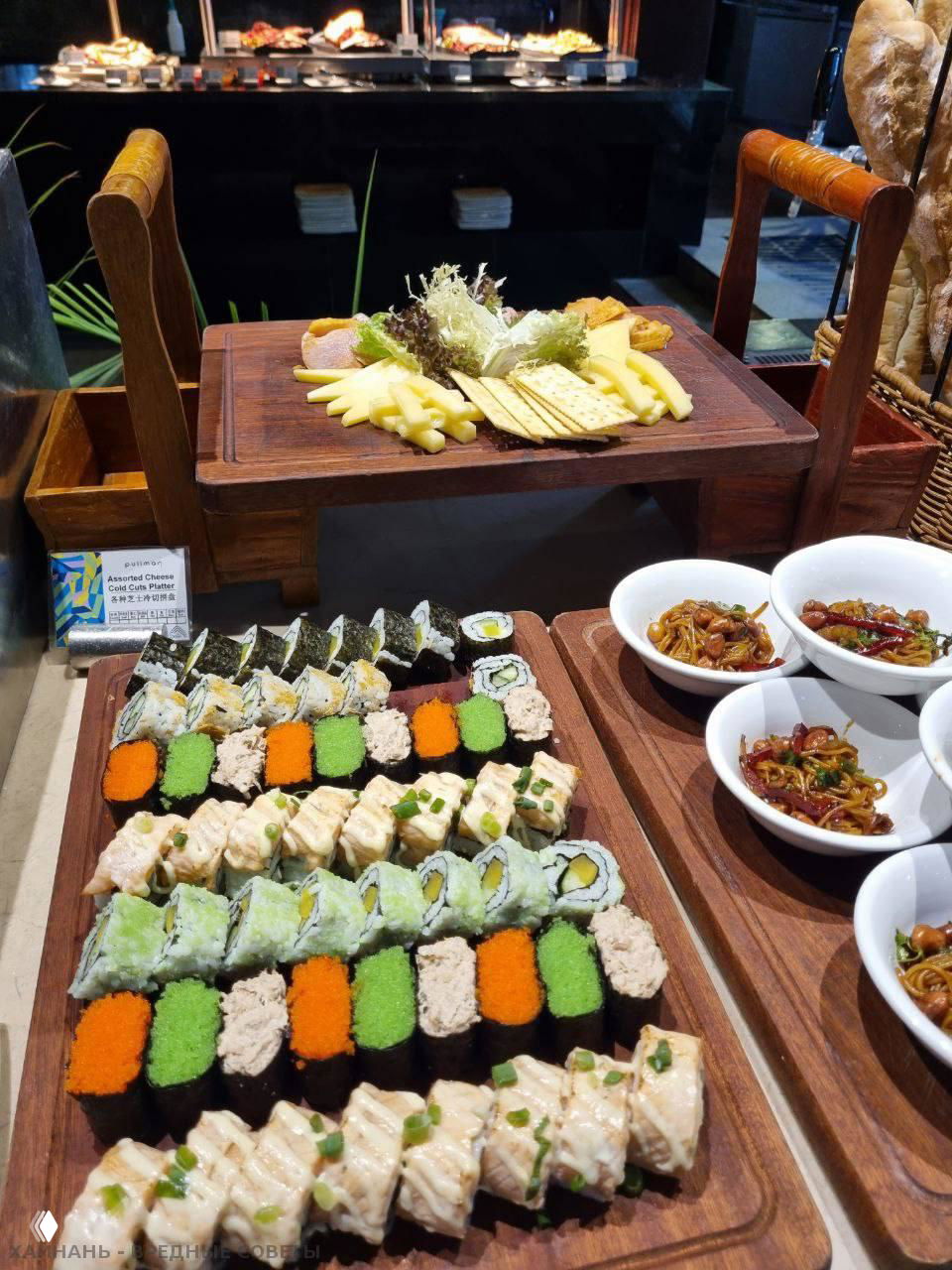 Деревянная доска с разнообразными роллами и суши: несколько видов роллов, нигири и украшения, часть зоны японской кухни на шведском столе отеля Pullman.