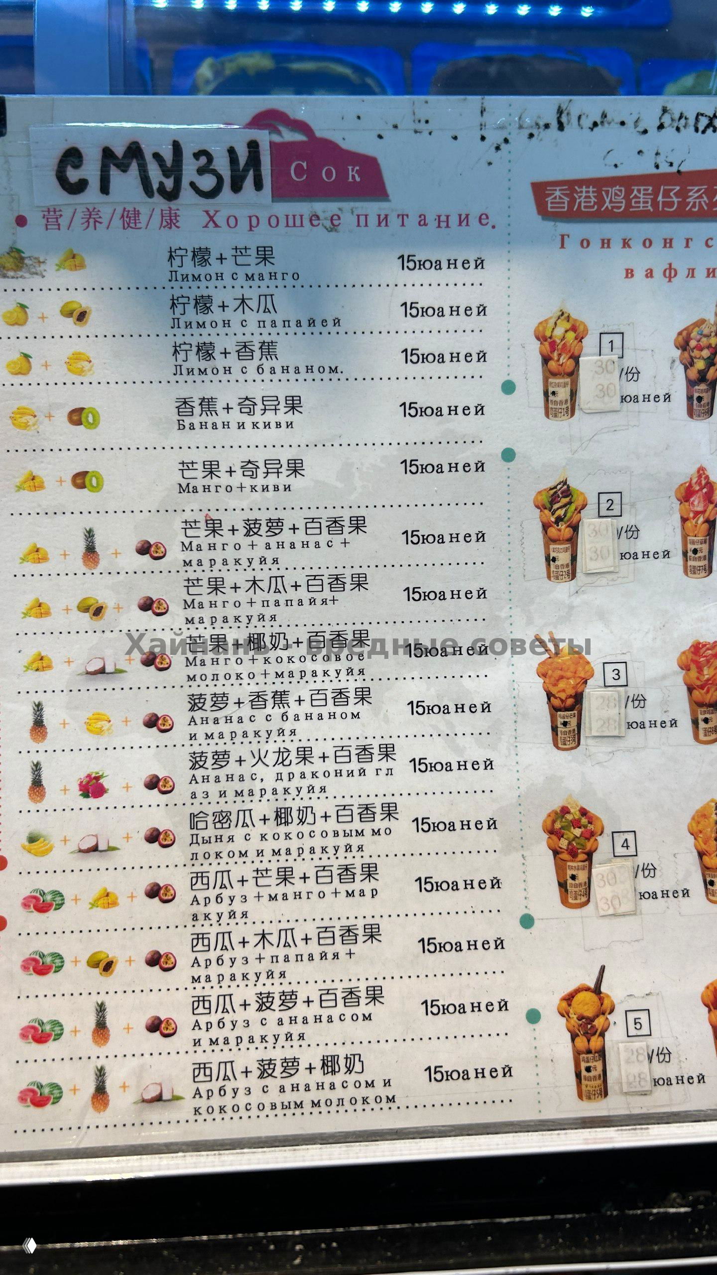 Ряд готовых гонконгских вафель с разнообразными начинками, выложенных на прилавке, каждая вафля украшена разными фруктами и соусами, видна рекламная лента.