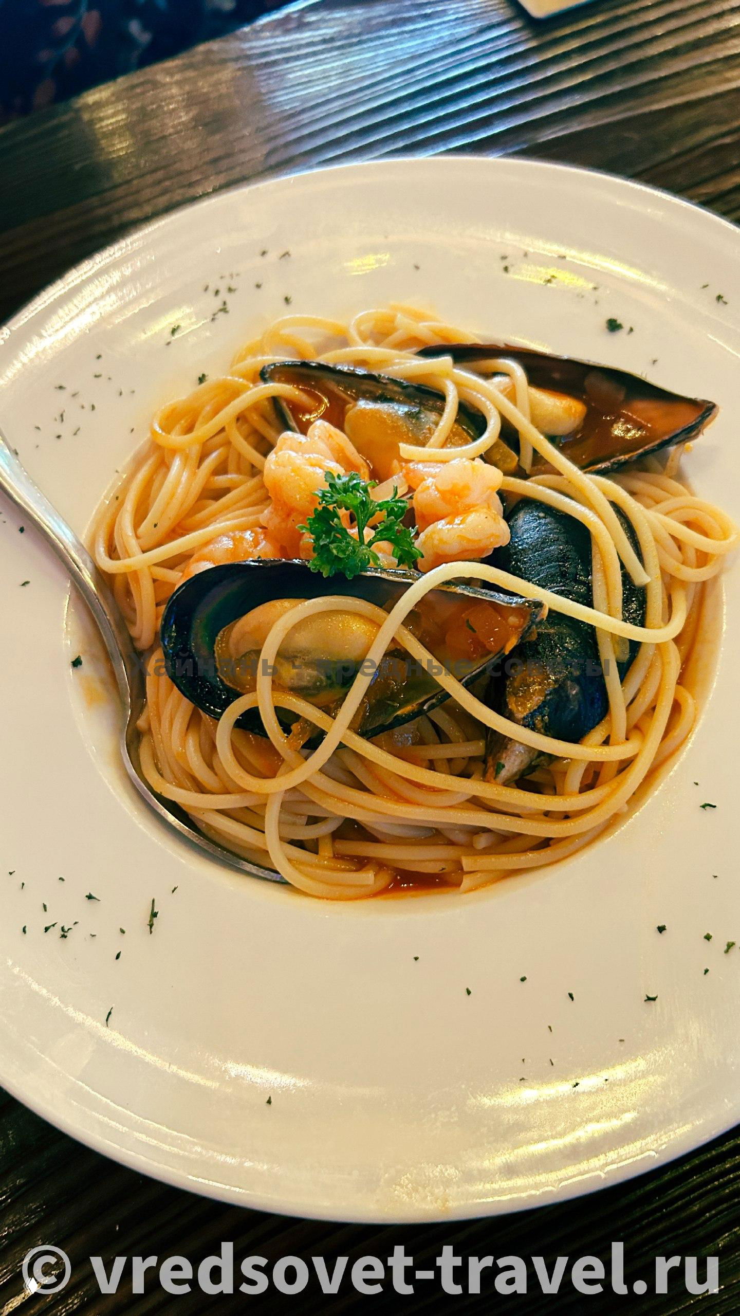 Паста с мидиями и креветками на белой тарелке: тонкие спагетти, морепродукты и свежая петрушка сверху, подача в европейском стиле.