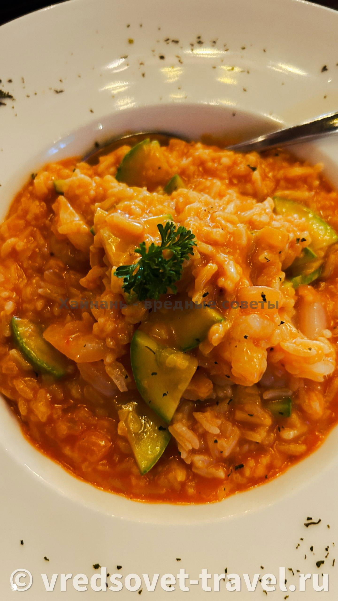 Рисотто или томатное ризотто с кубиками цуккини и зеленью на белой тарелке, кремовая текстура и украшение петрушкой в центре.