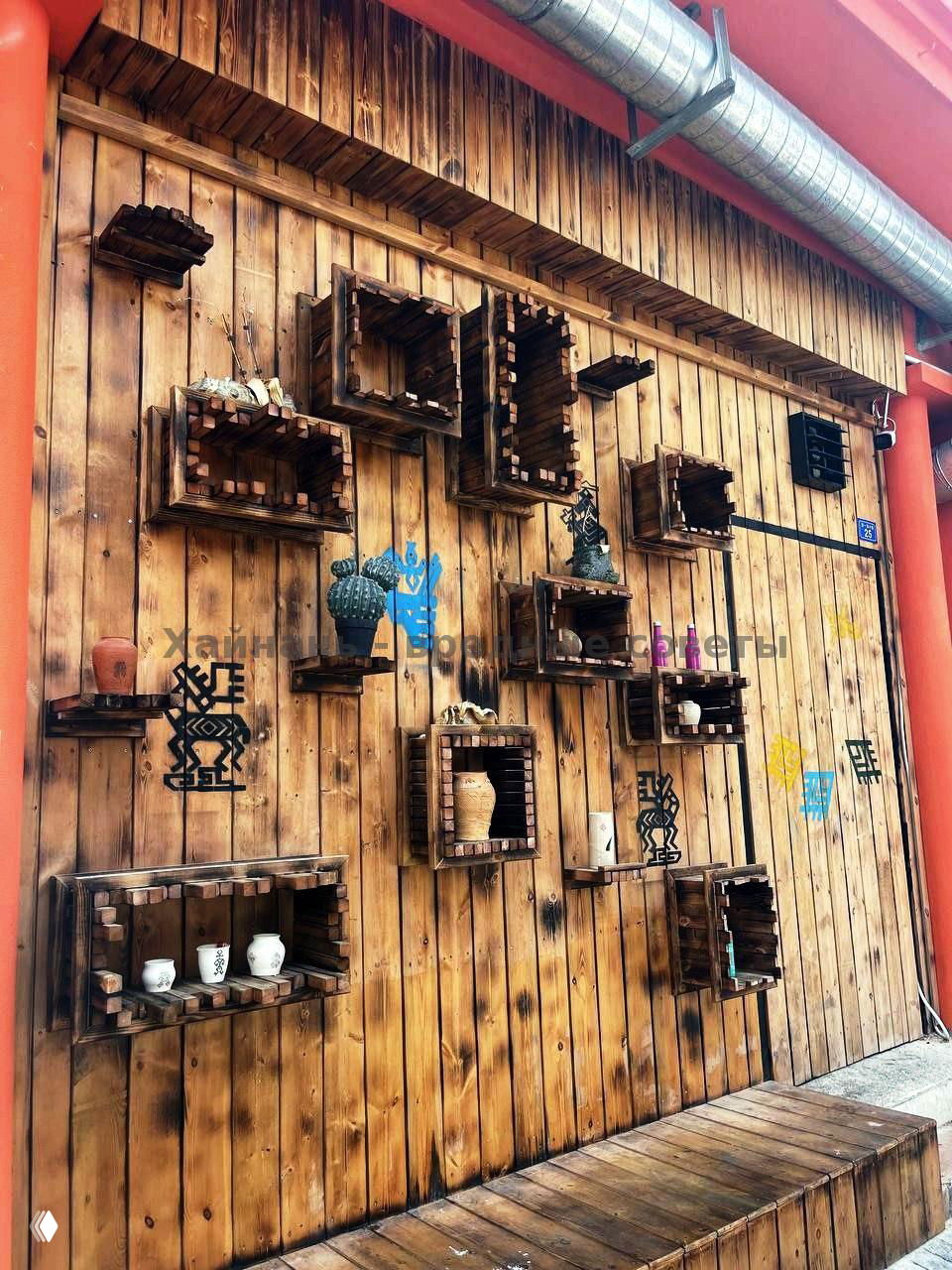 Деревянная декоративная стена с нишами и керамическими изделиями, оформленная в стиле рукодельного декора на фасаде одного из заведений Танья.