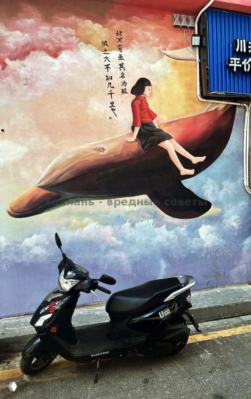 Стрит-арт на стене: девушка сидит на изображении кита, на переднем плане припаркован скутер — яркая фреска в туристическом квартале.
