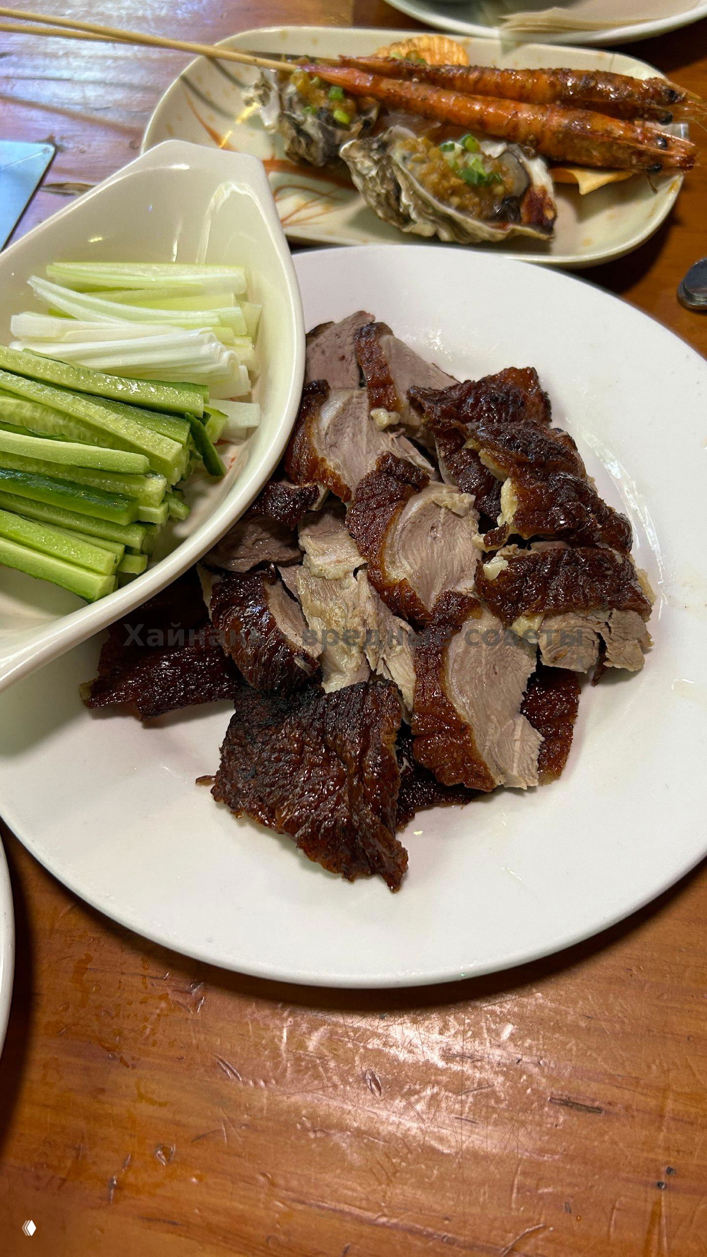 Фото стола с несколькими блюдами: креветки на шпажках, устрицы и нарезанное жареное мясо на тарелке в ресторане на Хайнане, вид крупным планом.