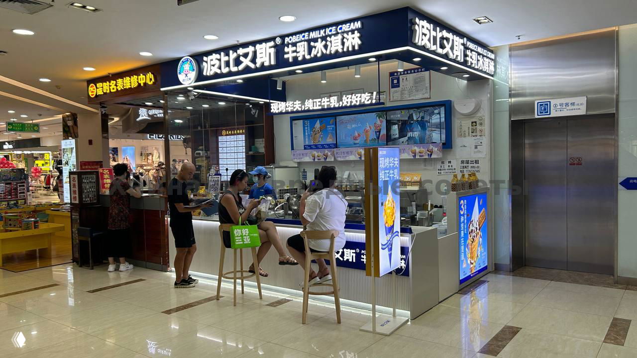 Фасад киоска мороженого в торговом центре на 3‑м этаже: вывеска, стойка и несколько посетителей сидят на высоких стульях у прилавка.