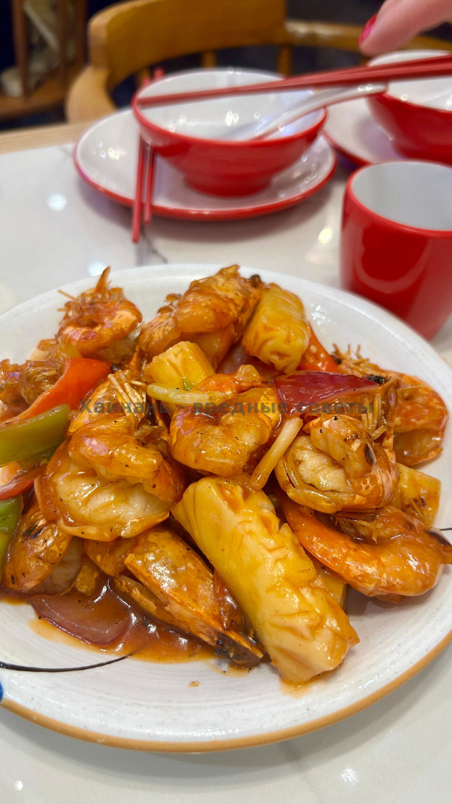 Тарелка с жареными креветками и кусочками ананаса крупным планом: соус блестит, видны палочки и сервировка на столе кафе в Ялонге.