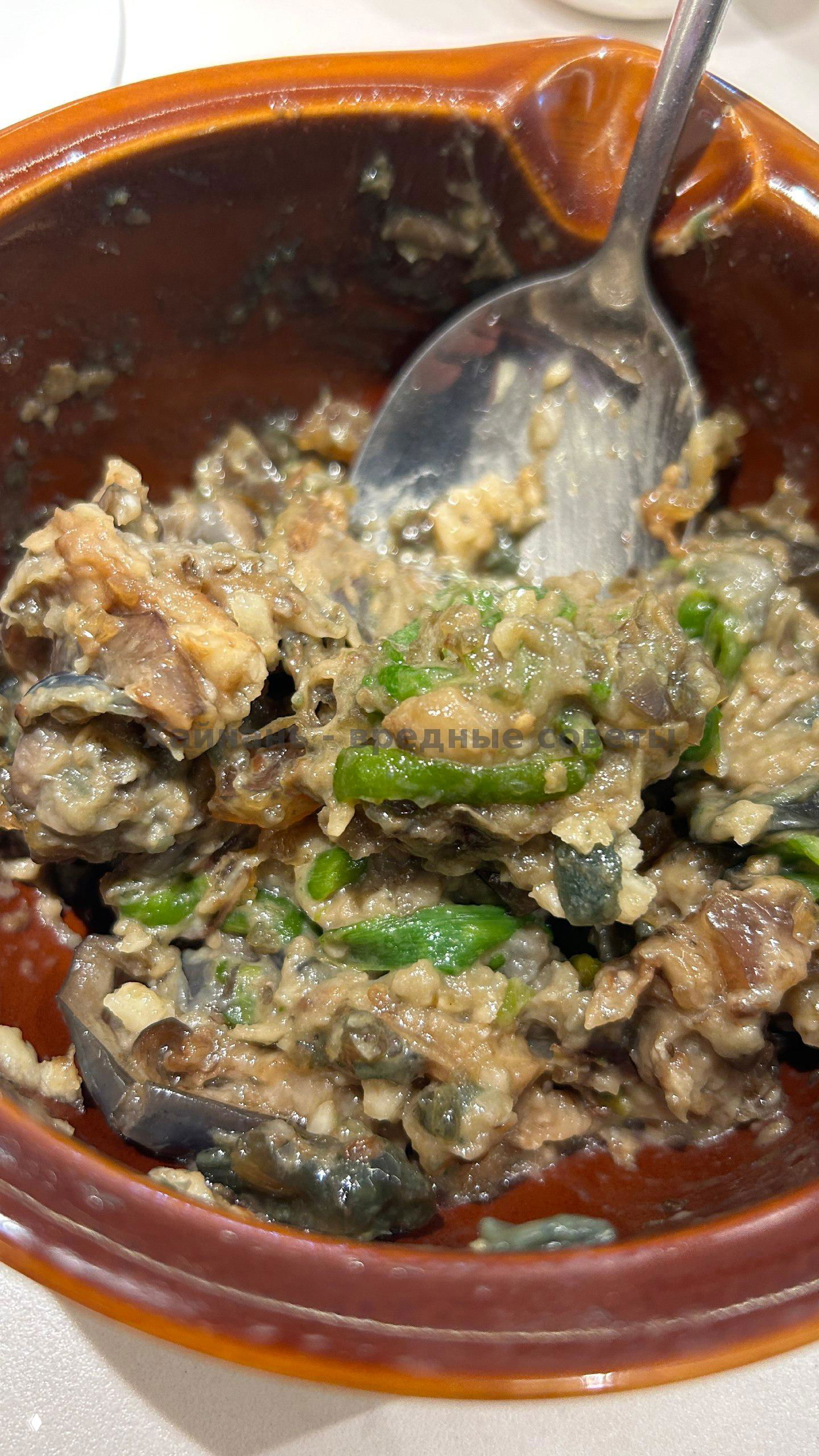 Крупный план блюда в глиняной миске: смешанные ингредиенты с зелёным луком, видно текстуру и соус крупным планом.