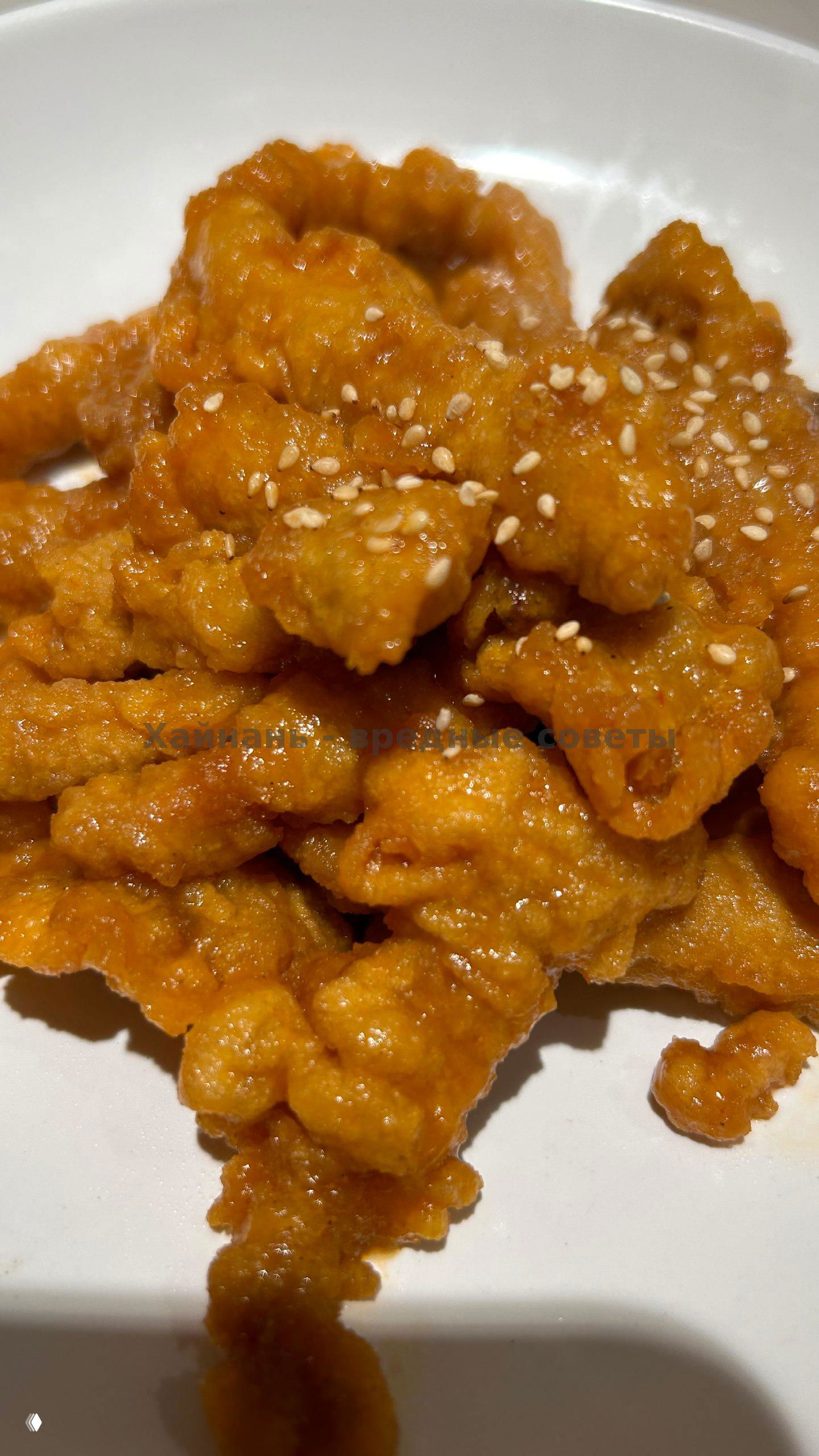 Крупный план жареных кусочков в золотистой панировке, посыпанных кунжутом, поданные на белой тарелке.