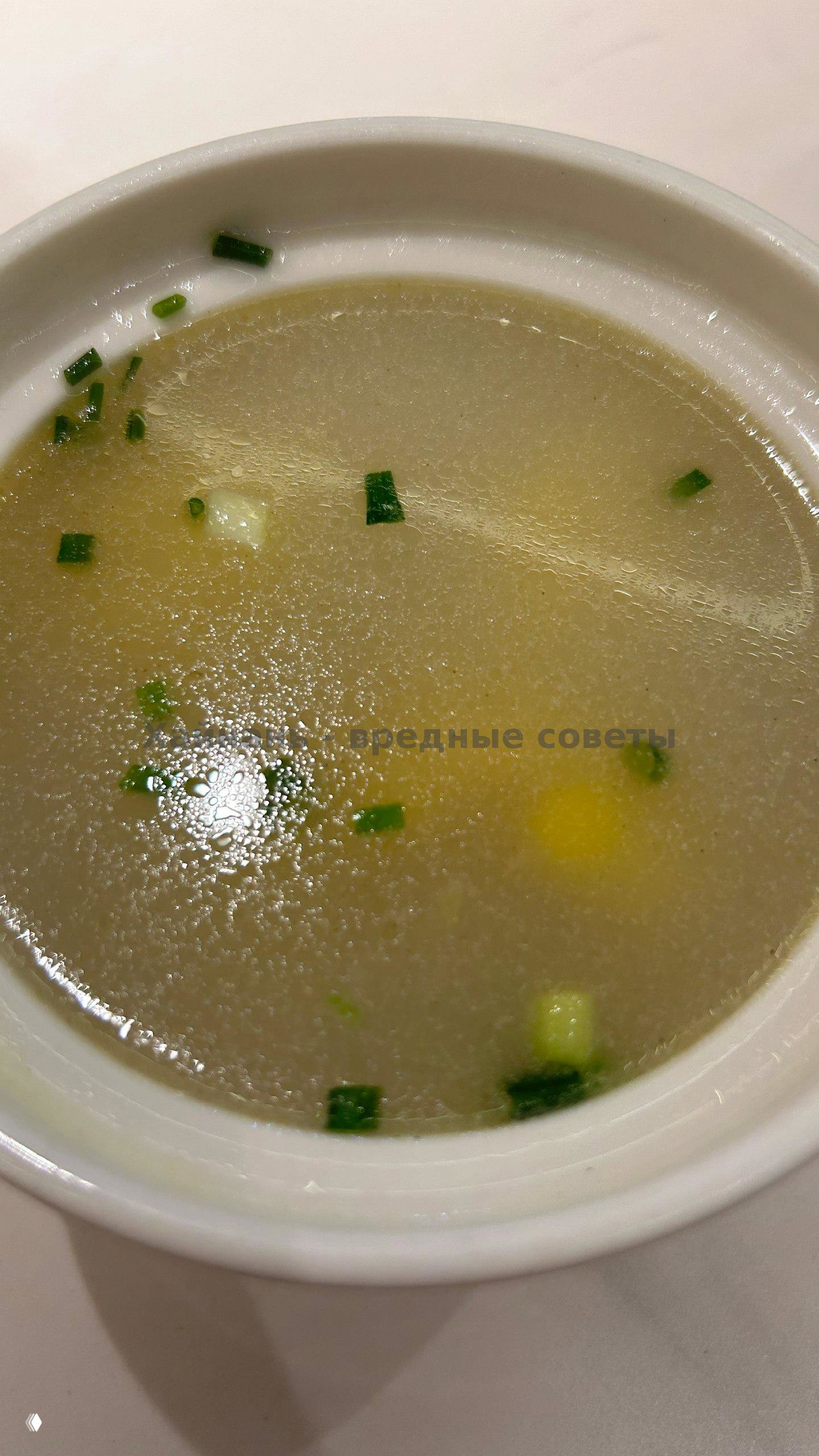 Белая миска с прозрачным бульоном и кусочками зелёного лука — лёгкий суп, видна поверхность жидкости и масло.