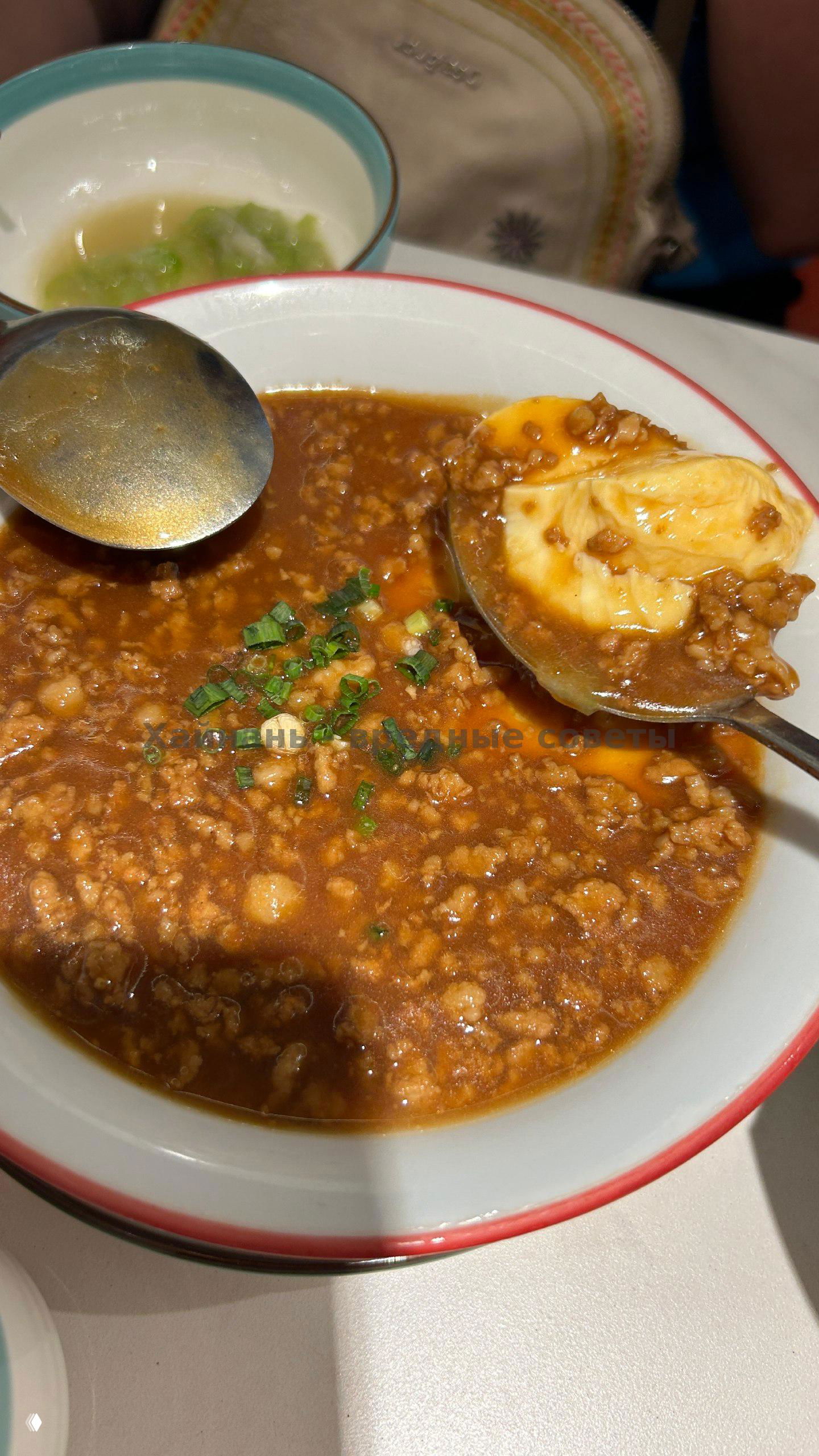 Тарелка с соусом и рубленым фаршем, в ложке виден мягкий кусок, похоже на яйцо в соусе с мясом и рубленой зеленью.