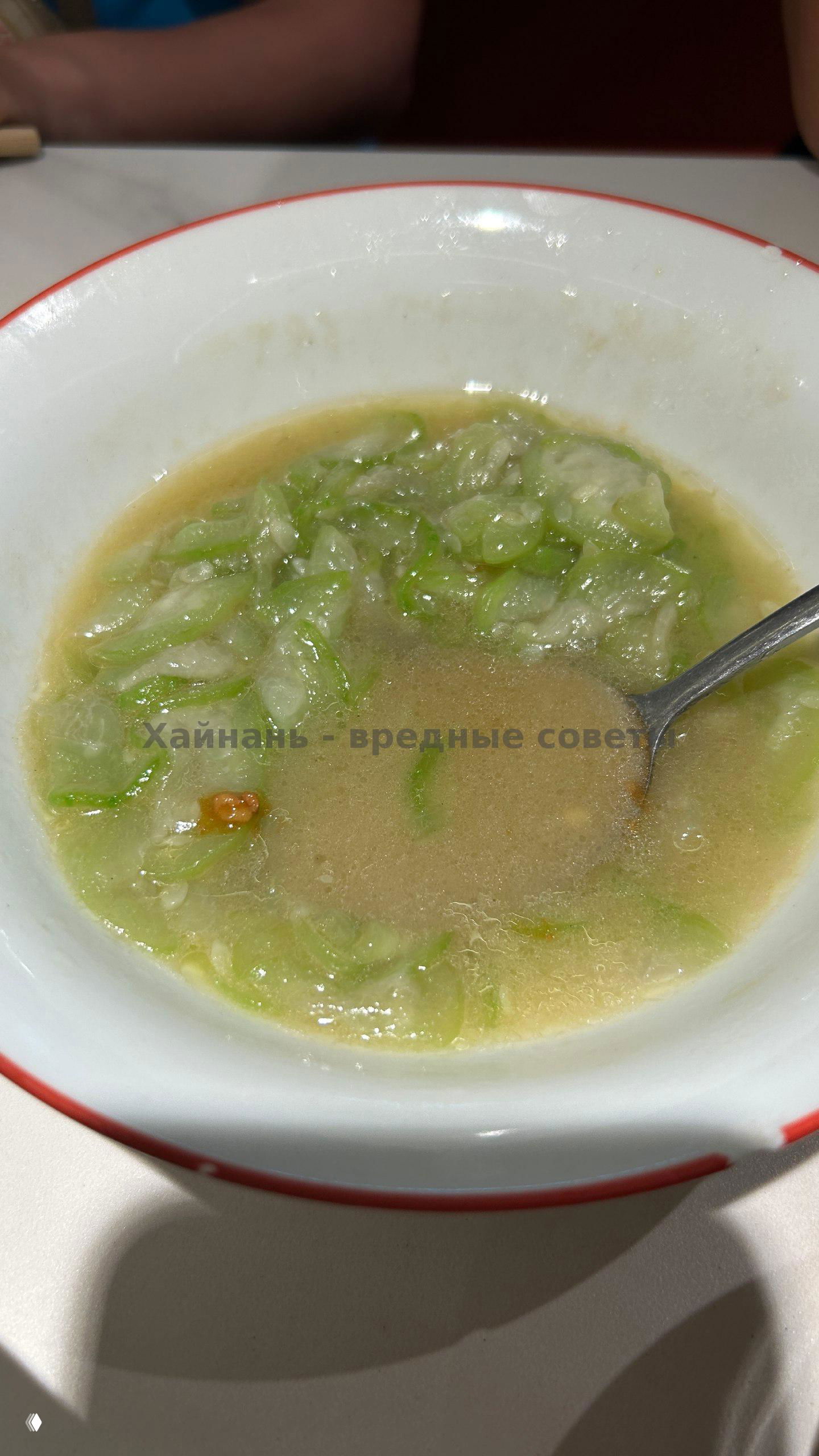 Миска с тушёными зелёными овощами в бульоне: кусочки зелени плавают в супе, видна ложка и часть стола.