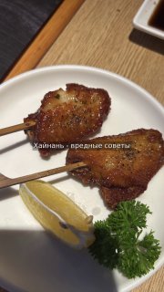 Близкий план жареных закусок на тарелке: две шпажки с обжаренным мясом, кусочек лимона и петрушка рядом, сервировка в кафе.