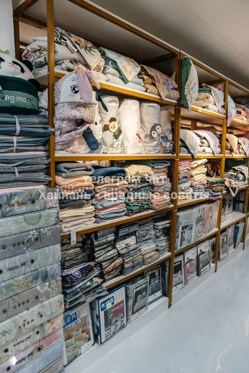 Стеллажи с постельным бельём, пледами и покрывалами: аккуратно сложенные комплекты разных цветов и узоров в широком ассортименте.