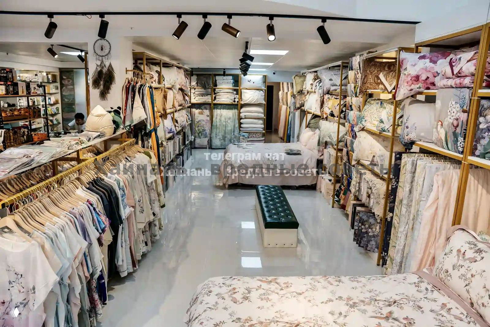 Общий вид торгового зала с кроватями, текстилем и одеждой: аккуратно расставленные полки и просторная планировка магазина.