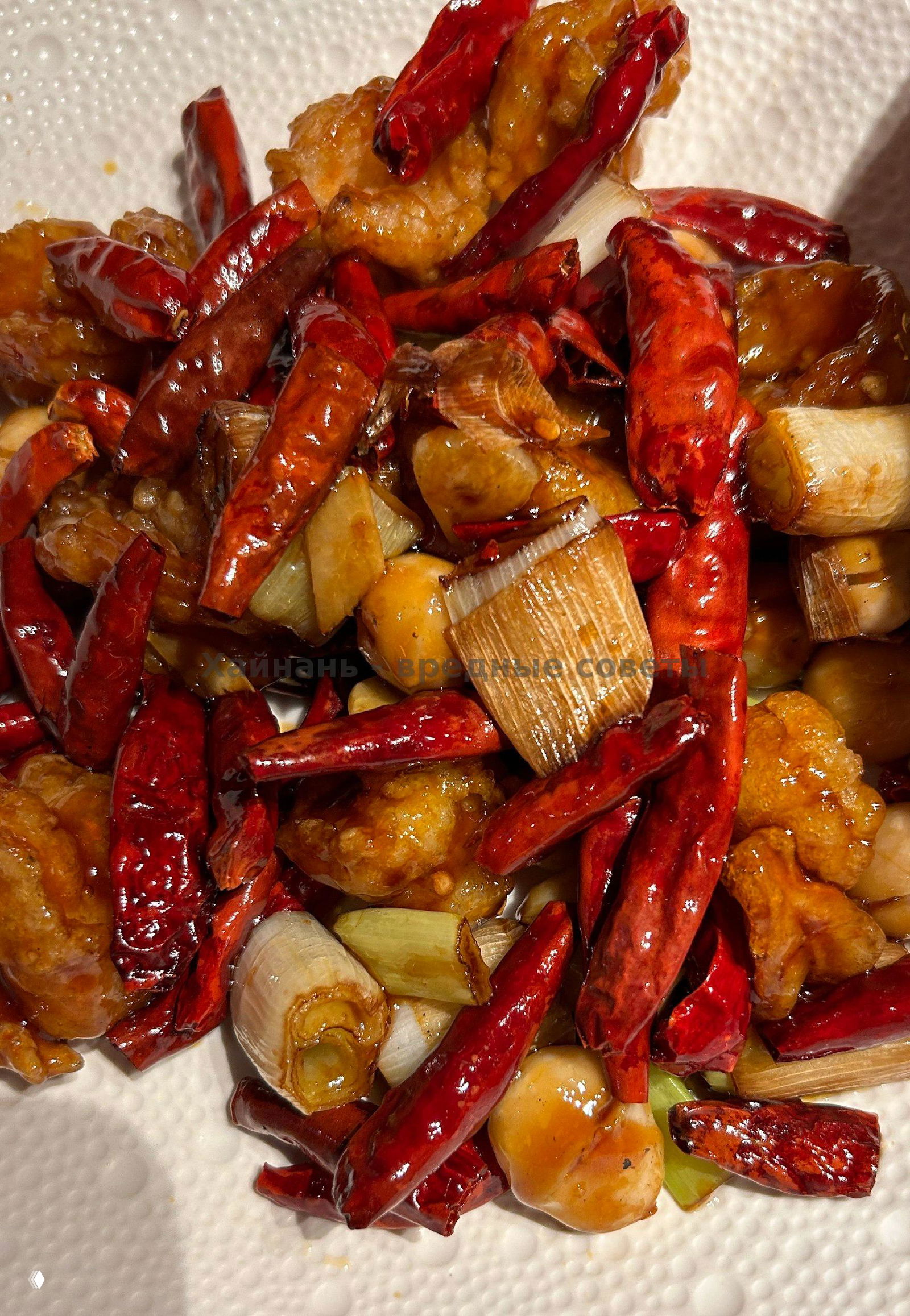 Блюдо с сухим перцем чили и кусочками жареного мяса или морепродуктов на белой тарелке — яркие красные стручки и украшения.