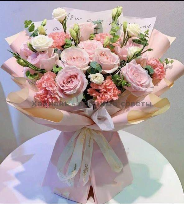 Пастельная композиция из розового и белого с лизиантусом и гвоздиками, упакованная в нежную бумагу и перевязанная атласной лентой, фото крупным планом.