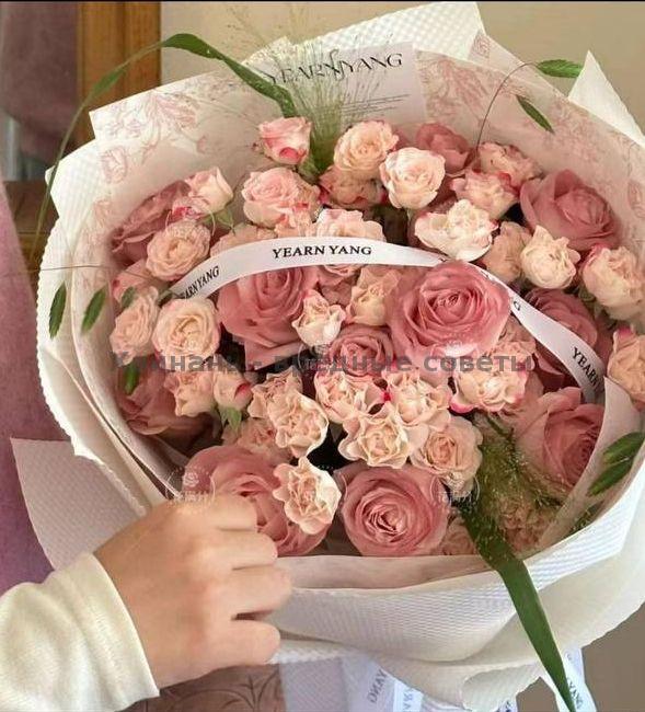 Круглый букет пудрово-розовых кустовых роз в цилиндрической шляпной коробке с брендовой лентой, аккуратно оформленный, фото показывает боковой ракурс композиции.