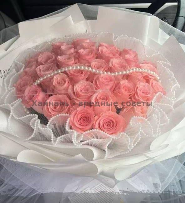 Роскошный букет ярко-розовых роз, упакованных слоями белой бумаги и украшенных жемчужной нитью, элегантный вариант для романтической доставки в отель.