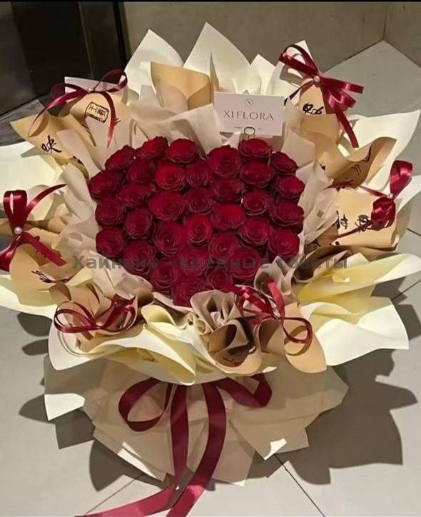 Большая композиция из тёмно-красных роз, сложенная в форме сердца с декоративными бантиками и золотистой упаковкой, эффектный подарок для торжеств и сюрпризов.