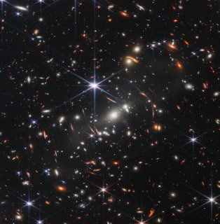 Кадр глубокого поля JWST: сотни удалённых галактик разнообразной яркости и заметные шестилучевые артефакты звёзд на тёмном космическом фоне.