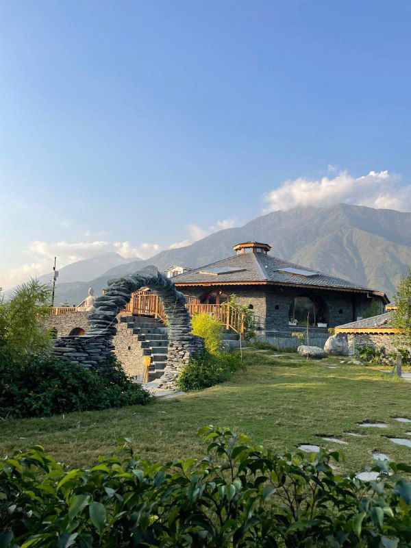 Каменные постройки и арочные проходы у подножия гор: вид на эко-отель или традиционную постройку в горной долине на фоне зелени.