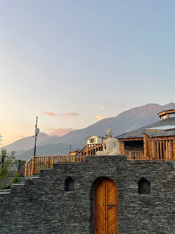 Деревянные террасы и домики на склоне гор при мягком закатном свете, силуэт гор на горизонте и спокойная атмосфера.