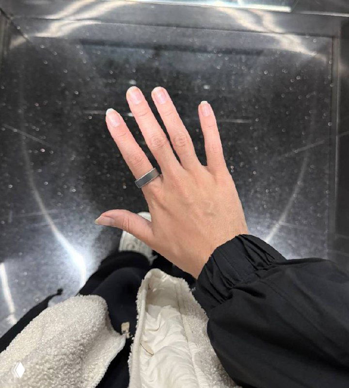 Фото руки автора с надетым кольцом Oura, снято сверху; видно металлическое кольцо на пальце, часть одежды и отражение пола вокруг.