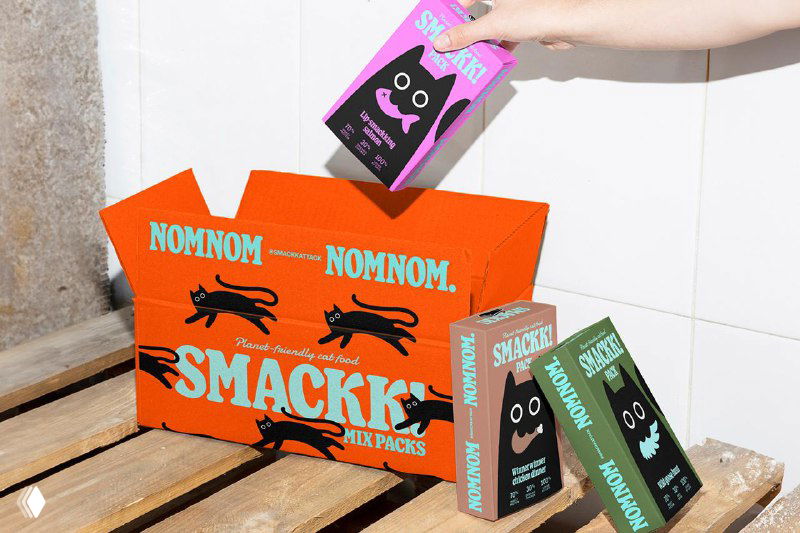 Коробки и наборы Smackk, открыт короб паковки с оранжевой графикой и повторяющимися мотивами бегущего кота и надписью NOMNOM на внутренней поверхности.