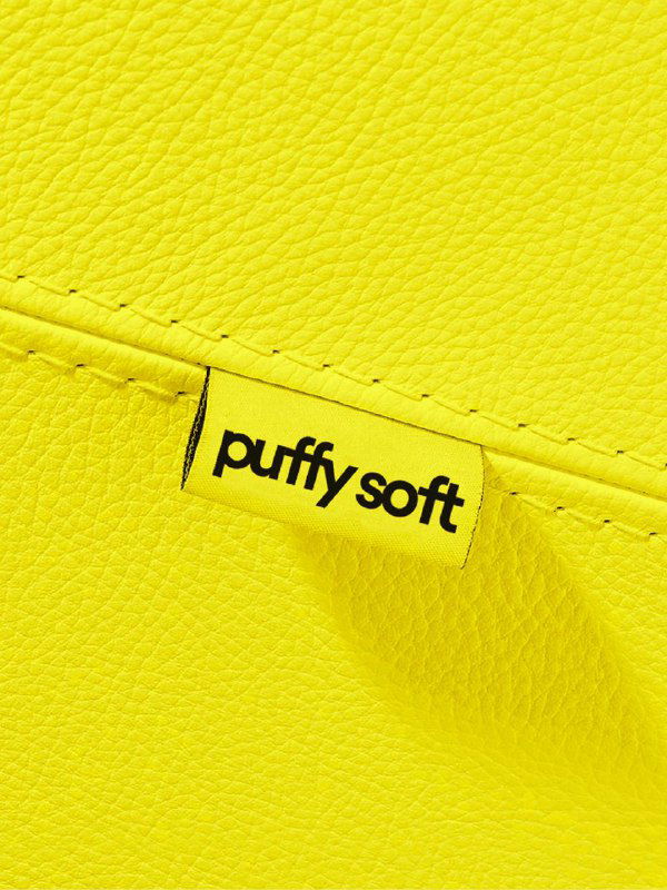 Крупный план жёлтой яркой текстуры с шитой биркой PuffySoft: деталь материалов и брендинга на поверхности надувной мебели.