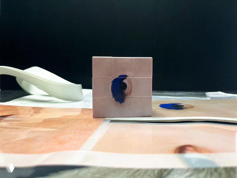 Студийный снимок макета: печатный разворот и куб с элементом айдентики — крупный фрагмент глаза и цветовой акцент на материале.