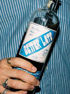 Крупный план бутылки с этикеткой «Better Life» в руке на фоне полосатой ткани; альтернативный или дополнительный дизайн-образ из съёмки бренда.