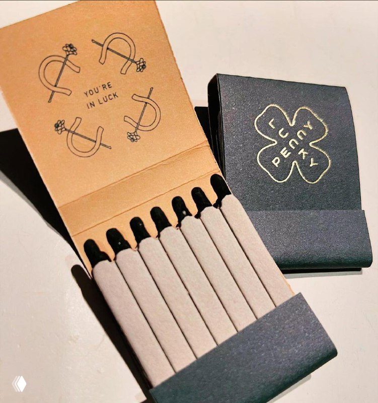 Минималистичная коробка спичек тёмно‑зелёного цвета с тонкими светло‑серым спичками и графическими эмблемами внутри, эстетика ретро‑брендинга.