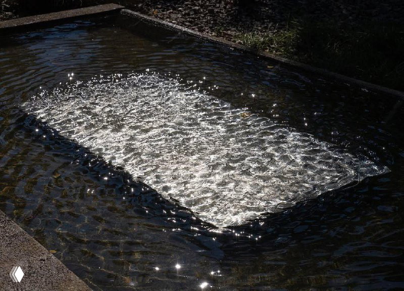 Пруд с движением воды, поверхность которого мерцает от рассеянного света — фрагмент водной световой инсталляции Лахлана Турчана.
