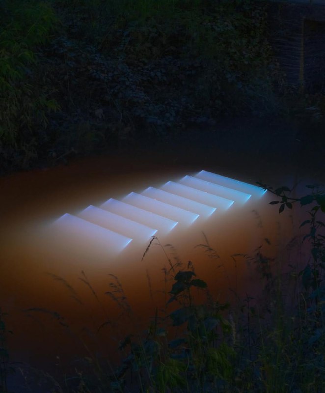 Подсвеченная ступенчатая конструкция, частично погружённая в воду — ночная сцена инсталляции Лахлана Турчана с мягким светом над водой.