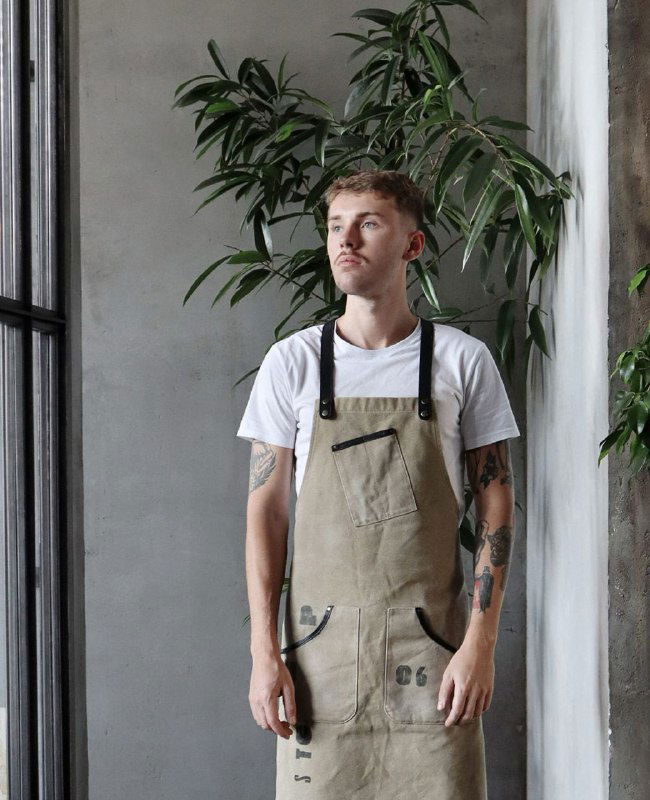 Фотография человека в фартуке работника ресторана на фоне зелёного растения и кирпичной стены — портрет персонала в стиле заведения.