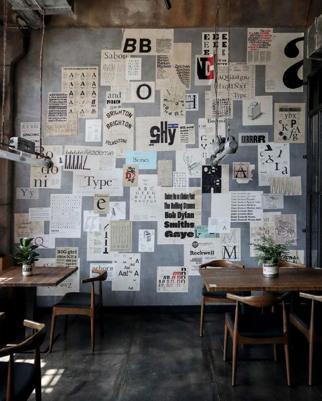 Общий вид зала ресторана с покрытой стеной коллажем из печатных листов, постеров и типографских экспериментов в индустриальном интерьере.