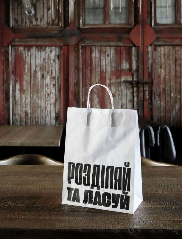 Бумажный пакет с кириллической надписью в грубой типографии на столе — пример фирменной упаковки ресторана в псевдовинтажном стиле.