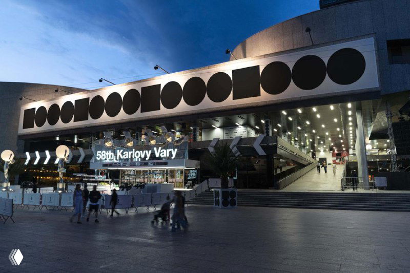 Ночной вид входа в кинотеатр/площадку фестиваля с длинной полосой круглых графических модулей и подсветкой у входа.