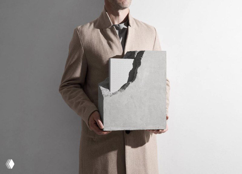Человек держит рельефный серый объект, имитирующий бетонный блок — акцент на материале, тактильности обложки и минималистичной эстетике издания.